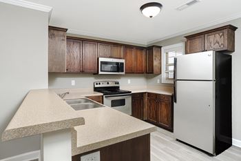 A kitchen with a refrigerator and wooden cabinets at The Meadows Apartments in Florence, AL